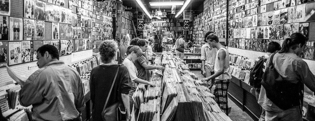 People browsing records in a record store with walls lined with vinyl records.
